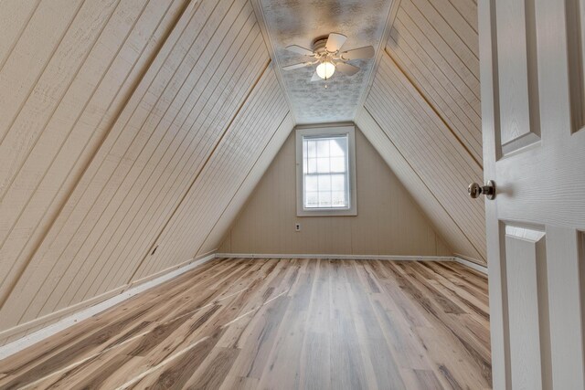 additional living space featuring lofted ceiling, ceiling fan, light wood-type flooring, and wood walls