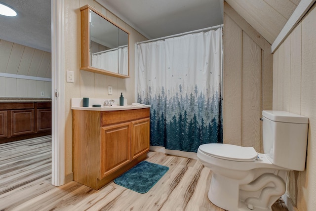 bathroom featuring wood walls, toilet, lofted ceiling, vanity, and hardwood / wood-style flooring