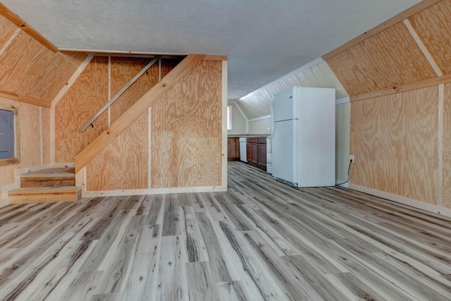 bonus room with wooden walls, a textured ceiling, vaulted ceiling, and light wood-type flooring