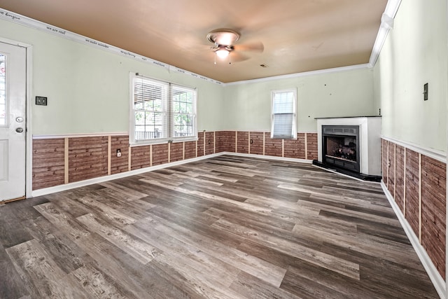 unfurnished living room featuring ceiling fan, ornamental molding, wooden walls, and hardwood / wood-style floors