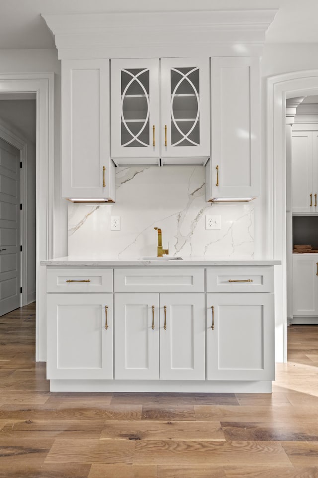 bar with backsplash, sink, white cabinets, and light wood-type flooring