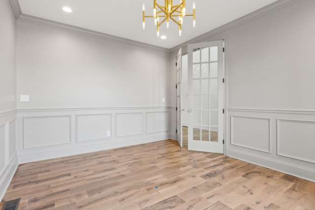 empty room featuring crown molding, a notable chandelier, light hardwood / wood-style floors, and french doors