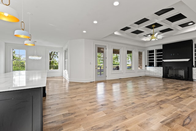 unfurnished living room with light hardwood / wood-style flooring, coffered ceiling, ceiling fan with notable chandelier, and a wealth of natural light