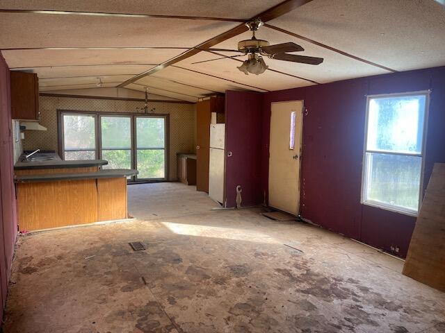 interior space with kitchen peninsula, ceiling fan, white fridge, and lofted ceiling