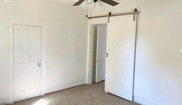 unfurnished bedroom featuring light colored carpet, ceiling fan, and a barn door