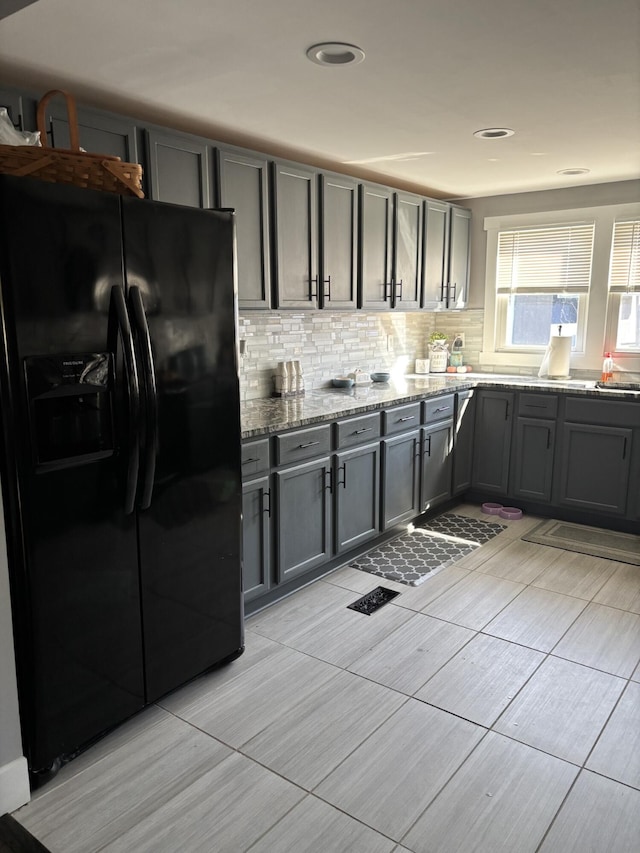 kitchen featuring black refrigerator with ice dispenser, light stone countertops, backsplash, and gray cabinets