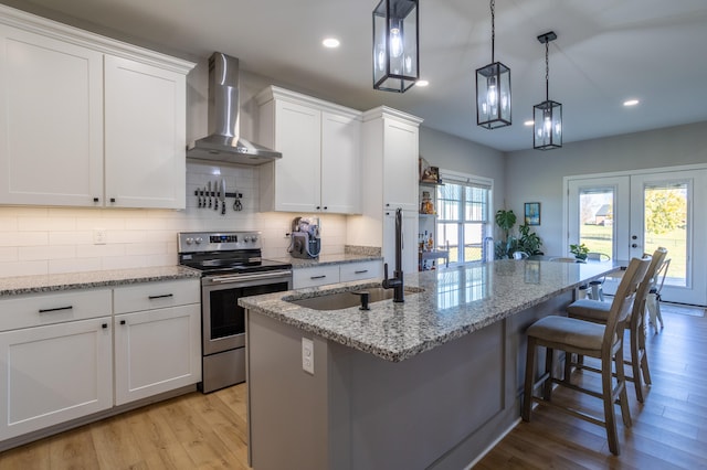 kitchen featuring stainless steel range with electric stovetop, wall chimney exhaust hood, white cabinetry, and light hardwood / wood-style floors