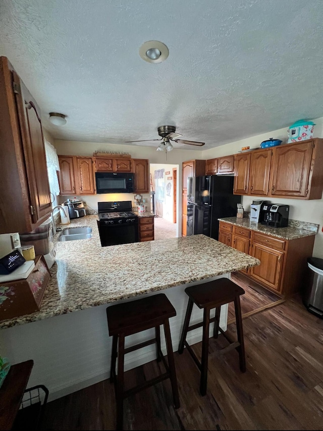 kitchen with sink, a kitchen breakfast bar, dark hardwood / wood-style floors, kitchen peninsula, and black appliances