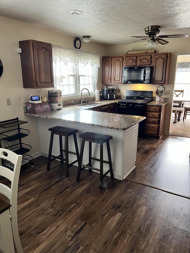 kitchen with ceiling fan, sink, a kitchen breakfast bar, kitchen peninsula, and black appliances