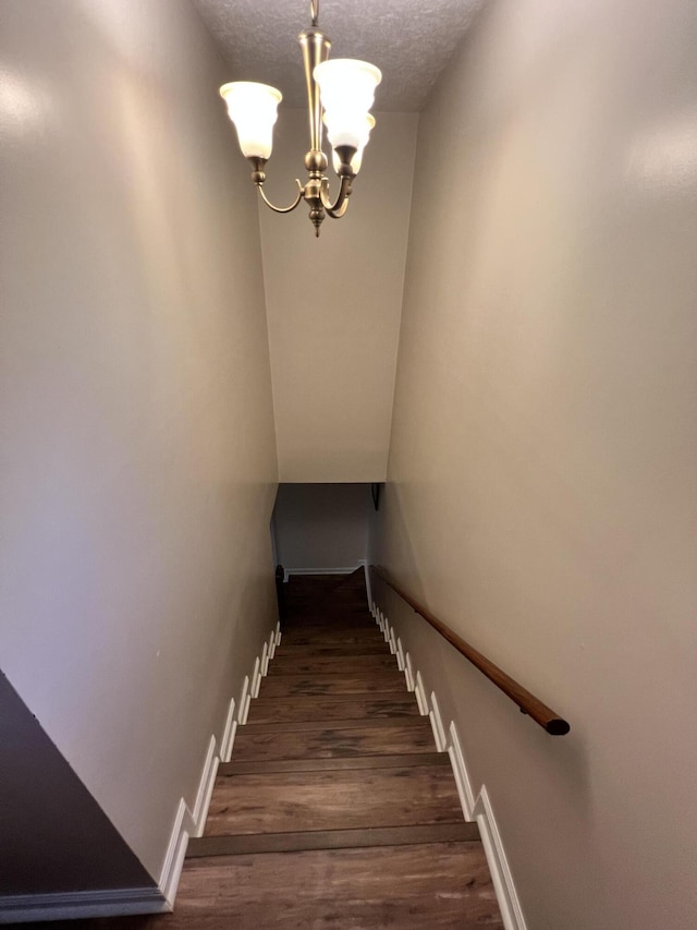 stairs with hardwood / wood-style floors, a textured ceiling, and a chandelier