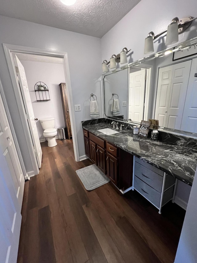 bathroom with hardwood / wood-style flooring, vanity, toilet, and a textured ceiling