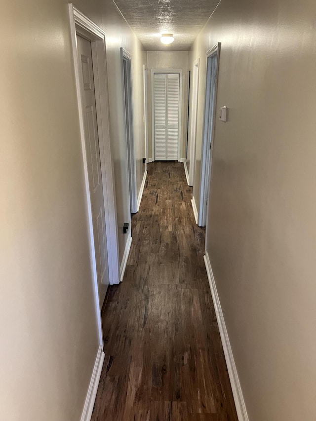 corridor with a textured ceiling and dark wood-type flooring