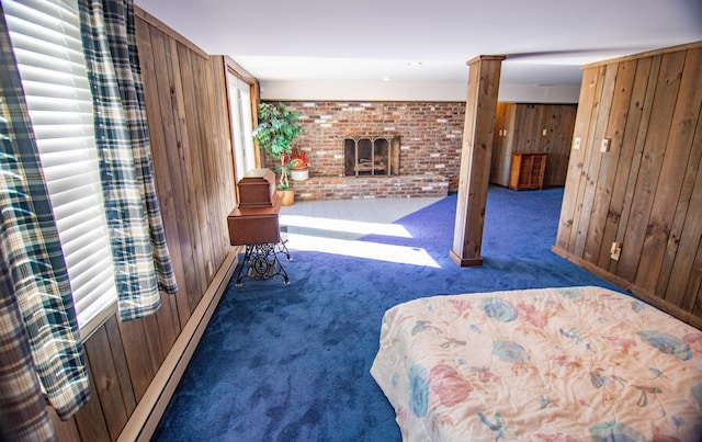 carpeted bedroom with wood walls, a baseboard heating unit, and a brick fireplace