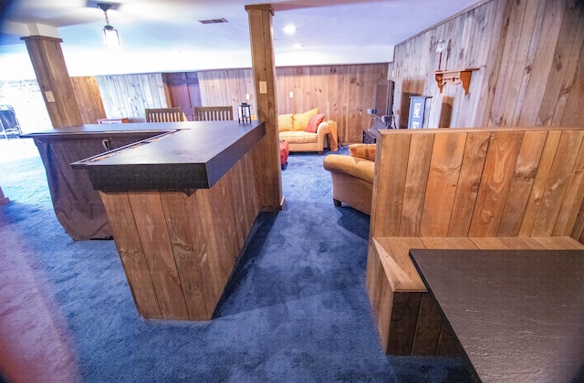 bar featuring ornate columns, wood walls, and dark carpet