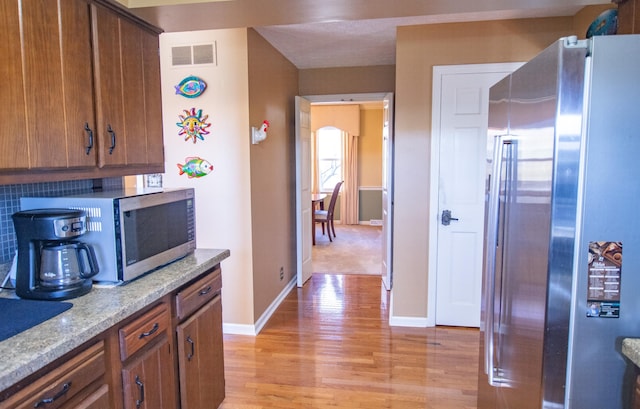 kitchen with stainless steel appliances, light hardwood / wood-style floors, light stone counters, and backsplash