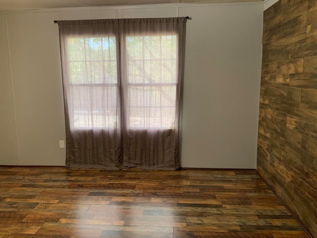 unfurnished room with dark wood-type flooring, wood walls, and crown molding