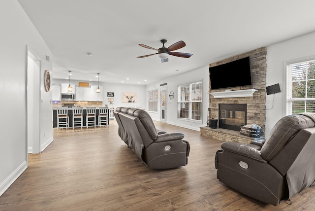 living room featuring hardwood / wood-style floors, a stone fireplace, and ceiling fan