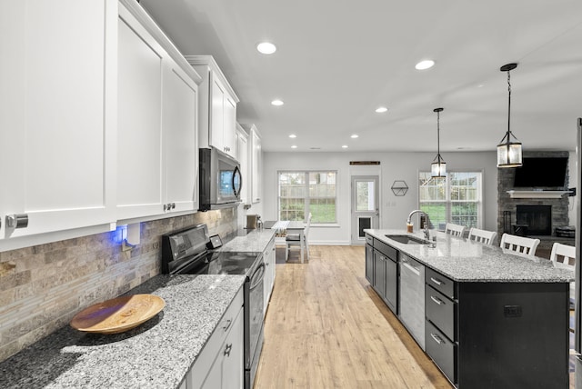 kitchen featuring a center island with sink, a stone fireplace, white cabinetry, appliances with stainless steel finishes, and sink