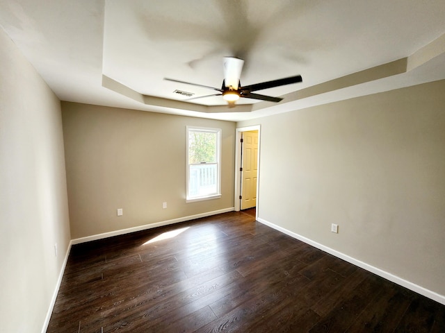 empty room with dark hardwood / wood-style flooring, a tray ceiling, and ceiling fan