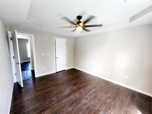 spare room featuring dark wood-type flooring, a tray ceiling, and ceiling fan