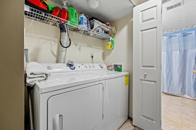 washroom with washing machine and dryer, light tile patterned flooring, and a textured ceiling