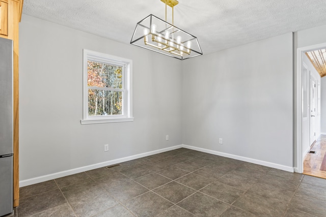 unfurnished dining area featuring a textured ceiling and dark tile patterned flooring