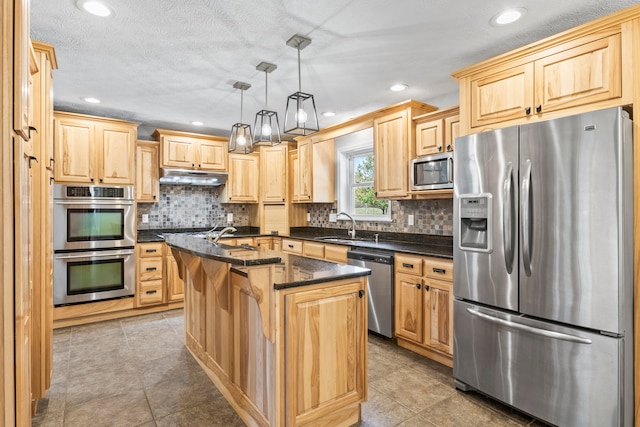 kitchen featuring stainless steel appliances, pendant lighting, light brown cabinets, sink, and a kitchen island with sink