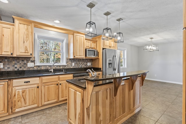 kitchen with sink, appliances with stainless steel finishes, tasteful backsplash, decorative light fixtures, and a kitchen island with sink