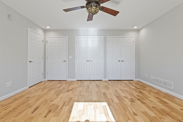 unfurnished bedroom with light hardwood / wood-style floors, ceiling fan, and two closets