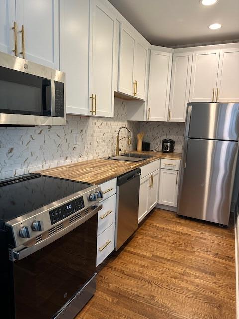 kitchen featuring appliances with stainless steel finishes, hardwood / wood-style flooring, white cabinetry, sink, and wood counters