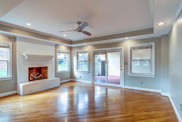 unfurnished living room with a raised ceiling, light hardwood / wood-style floors, ceiling fan, ornamental molding, and a fireplace