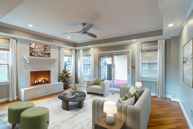 living room with wood-type flooring, a brick fireplace, ceiling fan, and crown molding