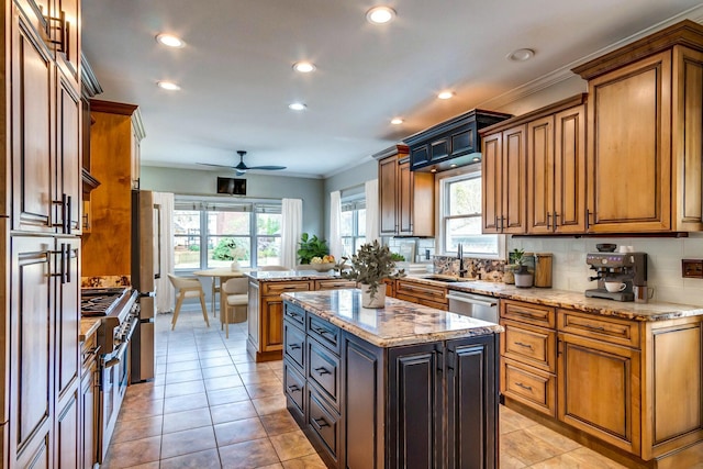 kitchen featuring light stone countertops, a center island, tasteful backsplash, appliances with stainless steel finishes, and ceiling fan