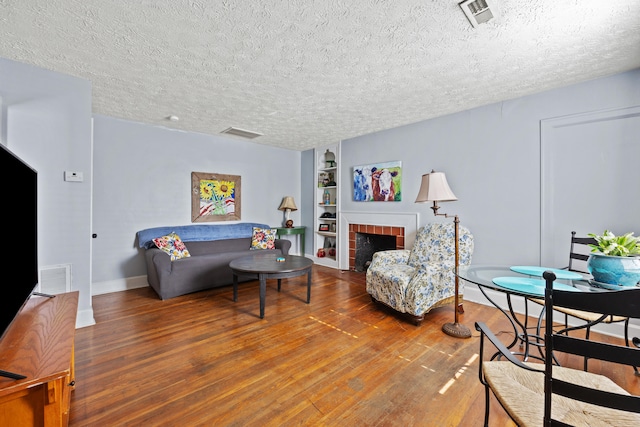 living room with a textured ceiling, wood-type flooring, and a brick fireplace