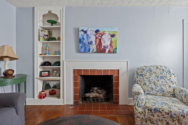 living room featuring a fireplace, a textured ceiling, built in shelves, and dark hardwood / wood-style flooring