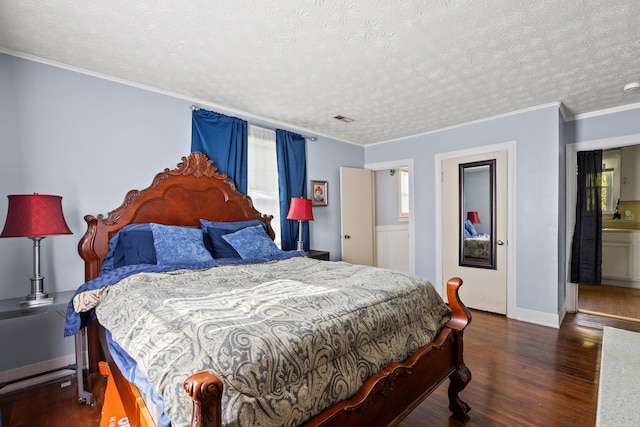 bedroom with dark wood-type flooring, a textured ceiling, ornamental molding, and ensuite bath