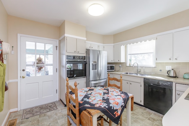 kitchen with white cabinets, black appliances, sink, and tasteful backsplash