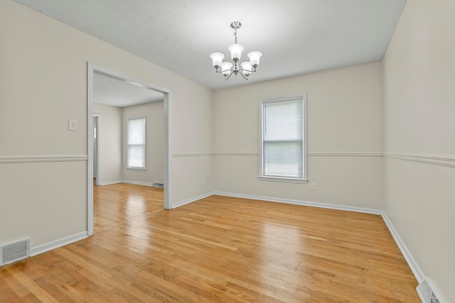 spare room with an inviting chandelier, a textured ceiling, and light hardwood / wood-style flooring