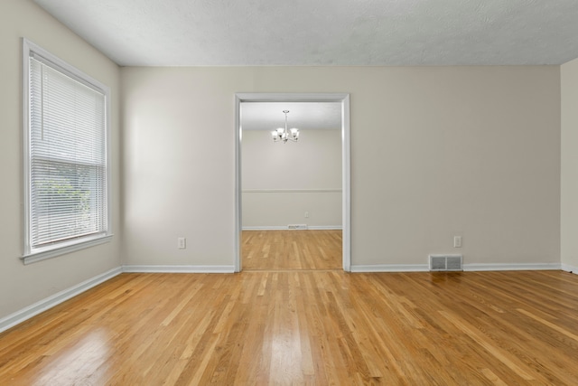 empty room featuring a chandelier, a textured ceiling, and light hardwood / wood-style floors