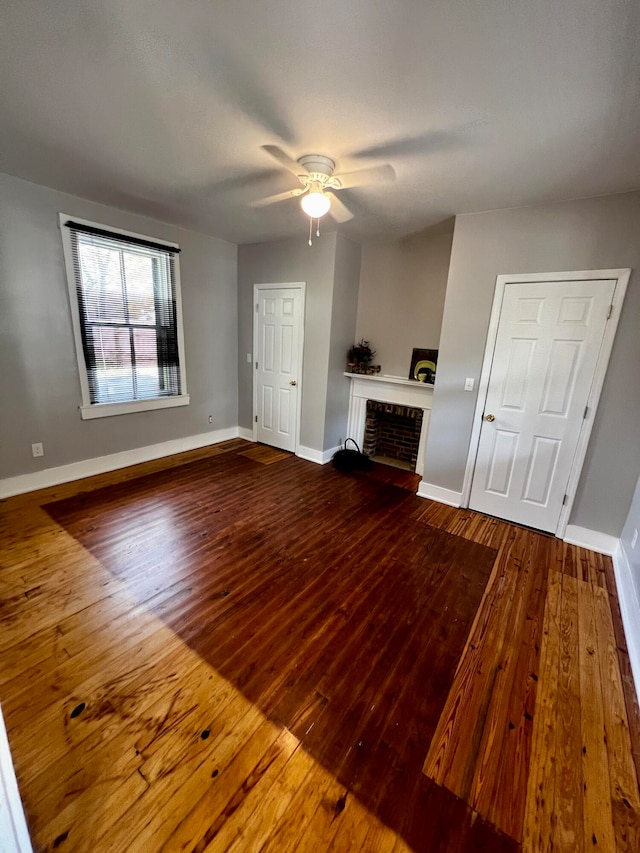 unfurnished living room featuring ceiling fan, wood-type flooring, and a brick fireplace