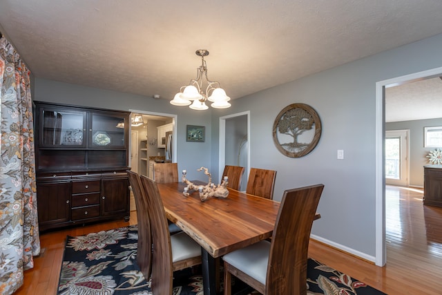 dining space featuring a textured ceiling, a notable chandelier, and light hardwood / wood-style flooring