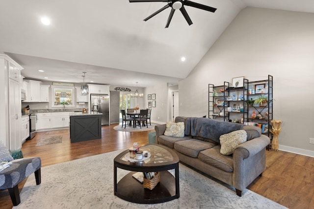 living room featuring ceiling fan with notable chandelier, dark wood-type flooring, sink, and high vaulted ceiling