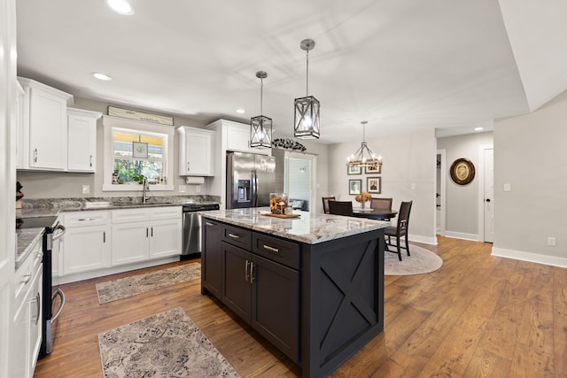 kitchen with light hardwood / wood-style floors, white cabinets, a kitchen island, appliances with stainless steel finishes, and decorative light fixtures