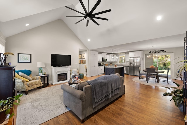 living room with ceiling fan with notable chandelier, wood-type flooring, and high vaulted ceiling