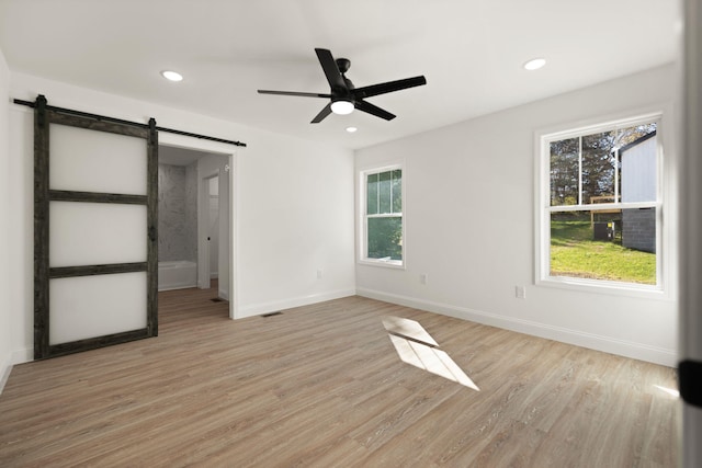 unfurnished bedroom featuring light wood-type flooring, a barn door, and ceiling fan