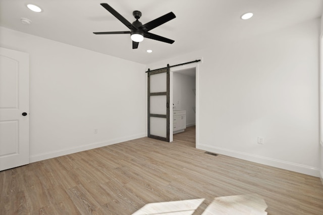 unfurnished bedroom featuring light hardwood / wood-style floors, a barn door, and ceiling fan