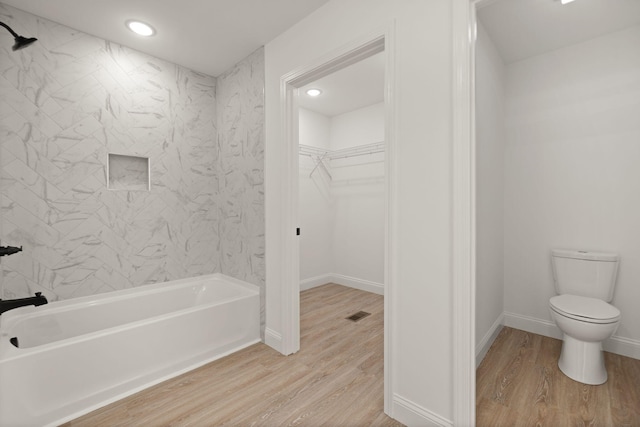 bathroom featuring wood-type flooring, toilet, and tiled shower / bath