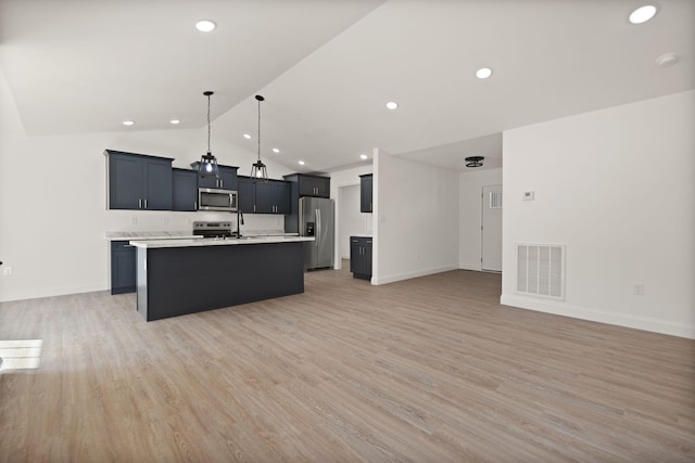 kitchen with light hardwood / wood-style floors, appliances with stainless steel finishes, an island with sink, hanging light fixtures, and vaulted ceiling