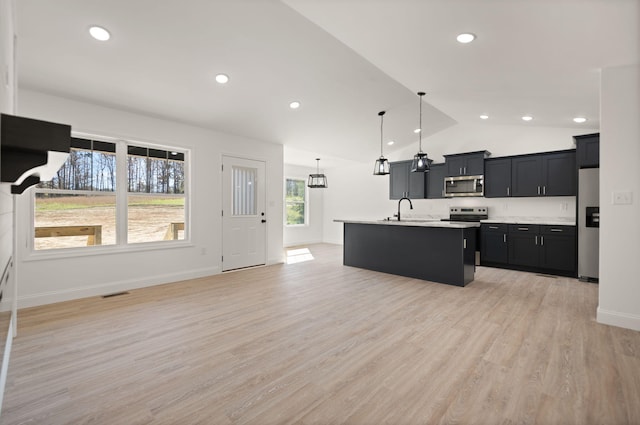 kitchen featuring lofted ceiling, light hardwood / wood-style flooring, an island with sink, pendant lighting, and appliances with stainless steel finishes