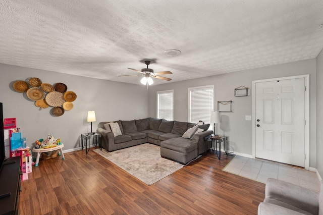 living room with a textured ceiling, ceiling fan, and dark wood-type flooring